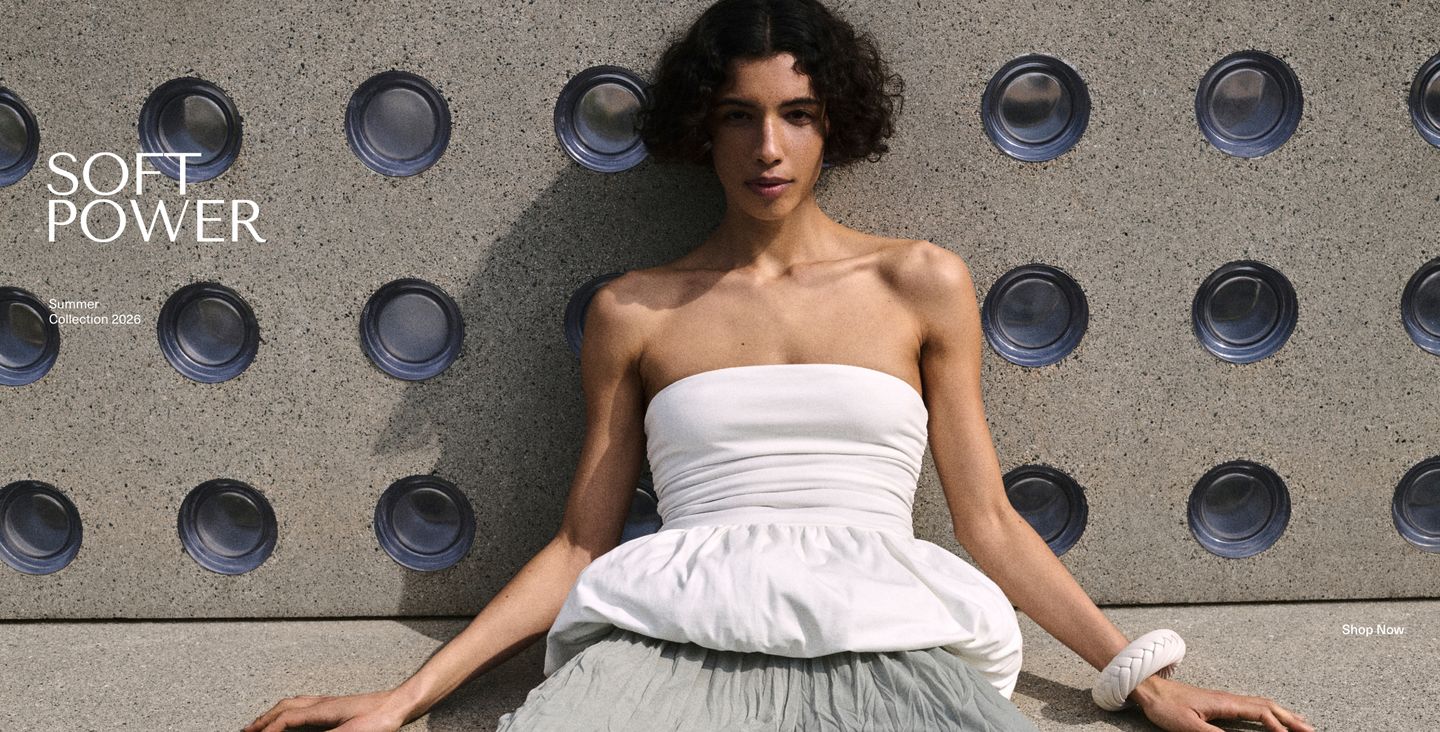 Model in white strapless top and gray skirt sits against textured wall. Text reads "Soft Power, Summer Collection 2026. Shop Now."