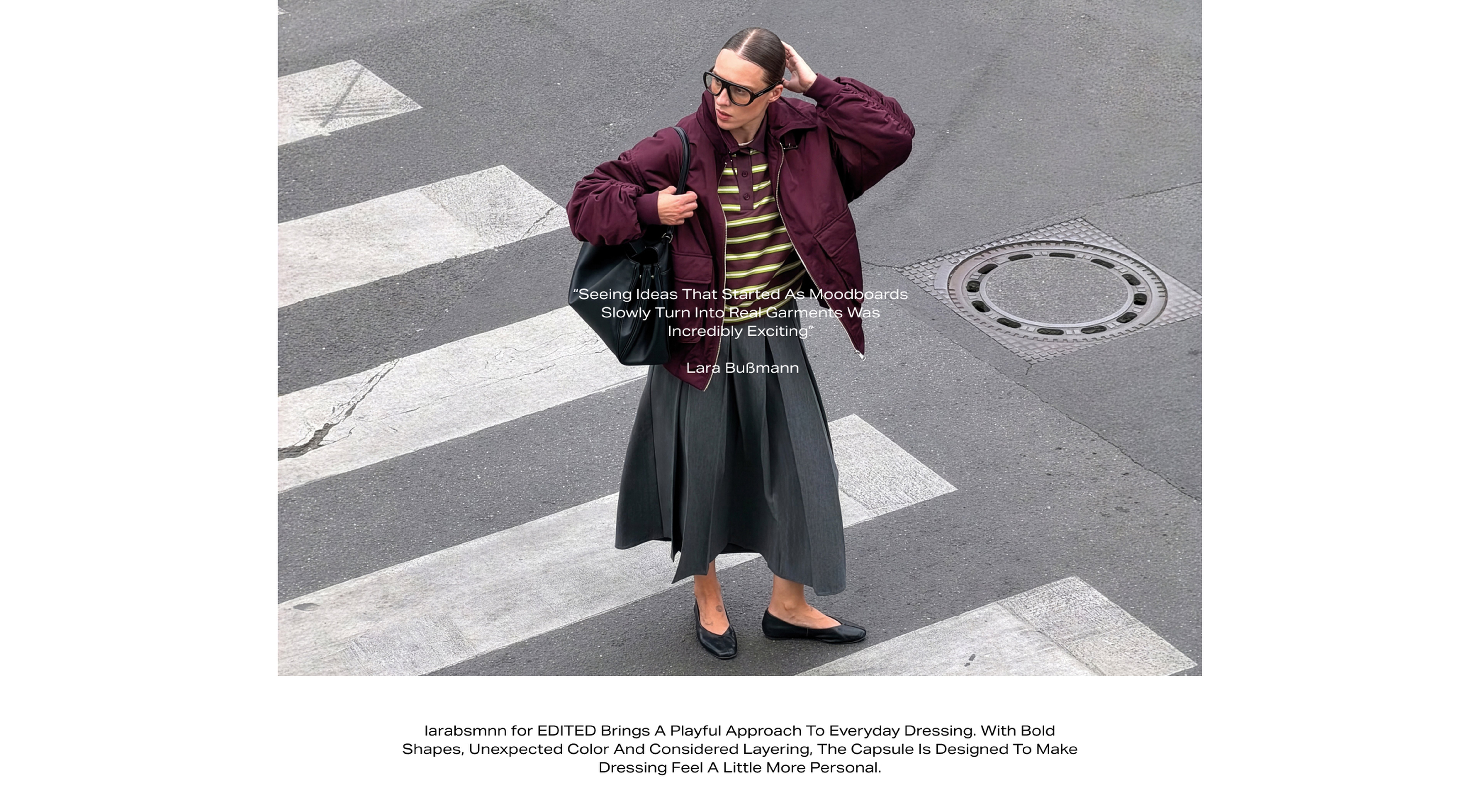 Woman in a burgundy jacket and striped shirt, crossing a city street on a pedestrian crossing, holding a black bag.