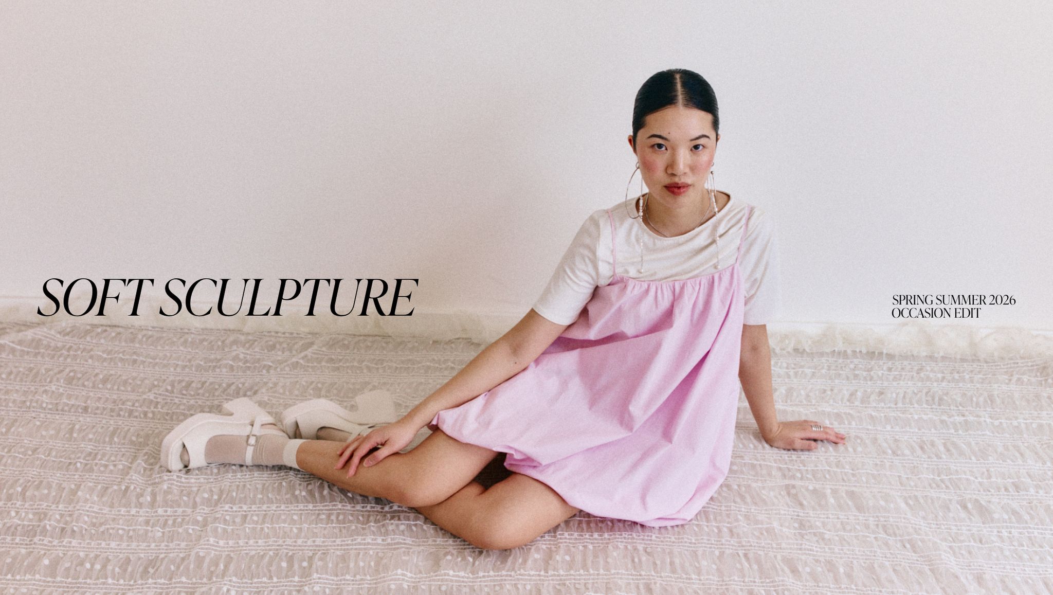 Woman in a pink dress sits on a patterned rug. The words "Soft Sculpture" and "Spring Summer 2026 Occasion Edit" appear in the image.