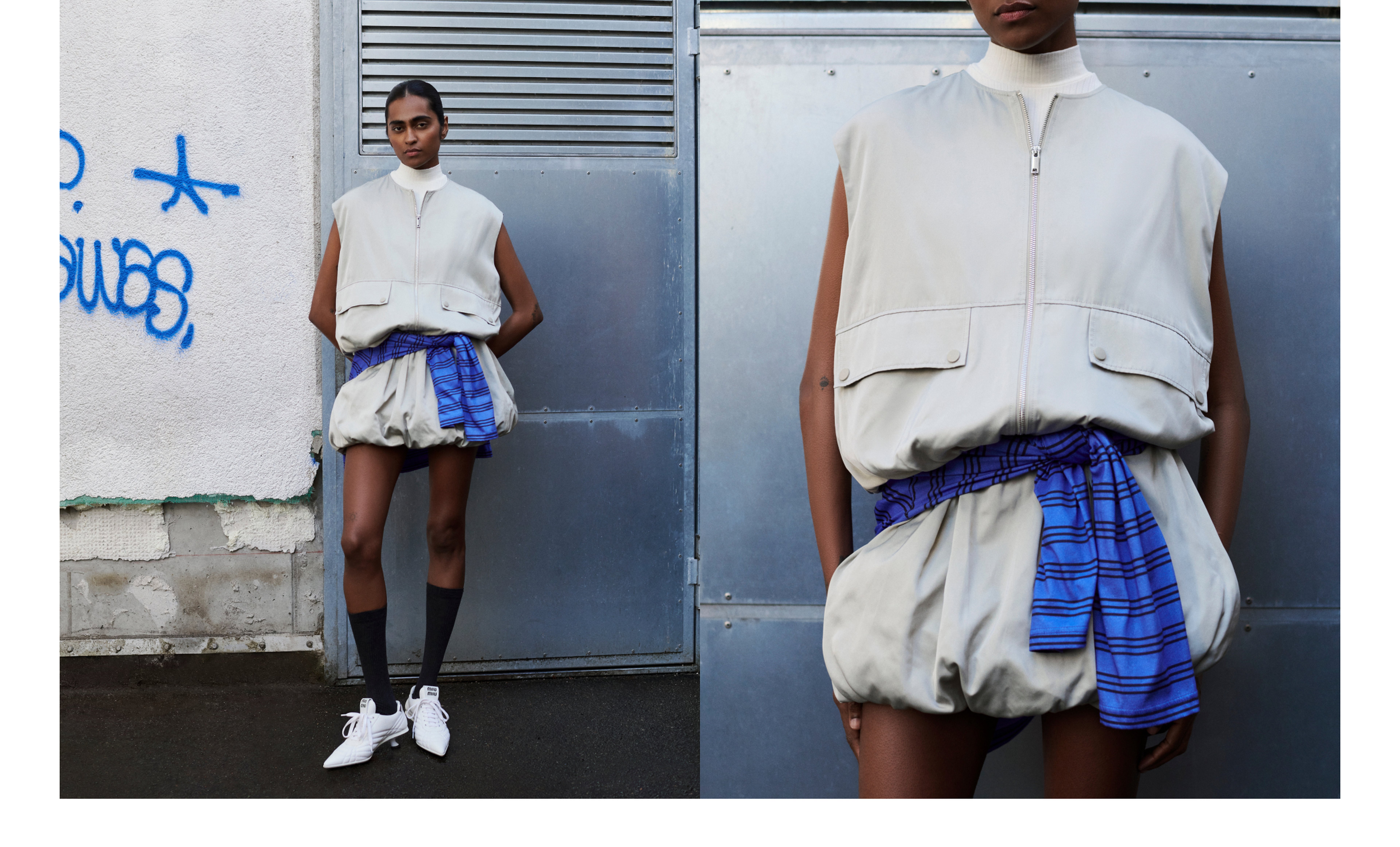 Fashionable model in a sleeveless beige outfit with a blue plaid accent, black socks, and white shoes, standing against an industrial backdrop.