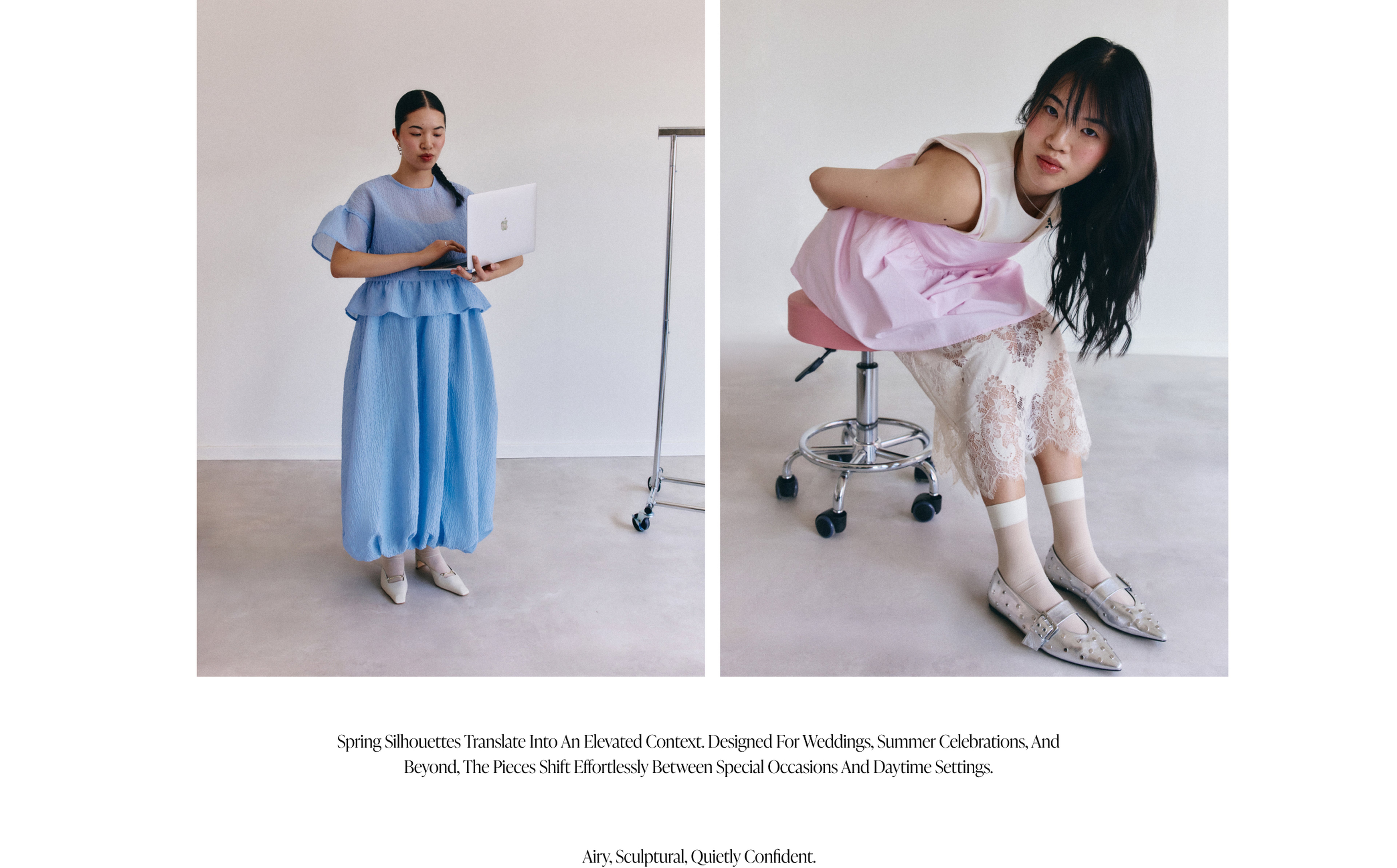 Two women in airy outfits; one in blue with a laptop, the other in pink and lace, sitting on a stool. Minimalist setting.