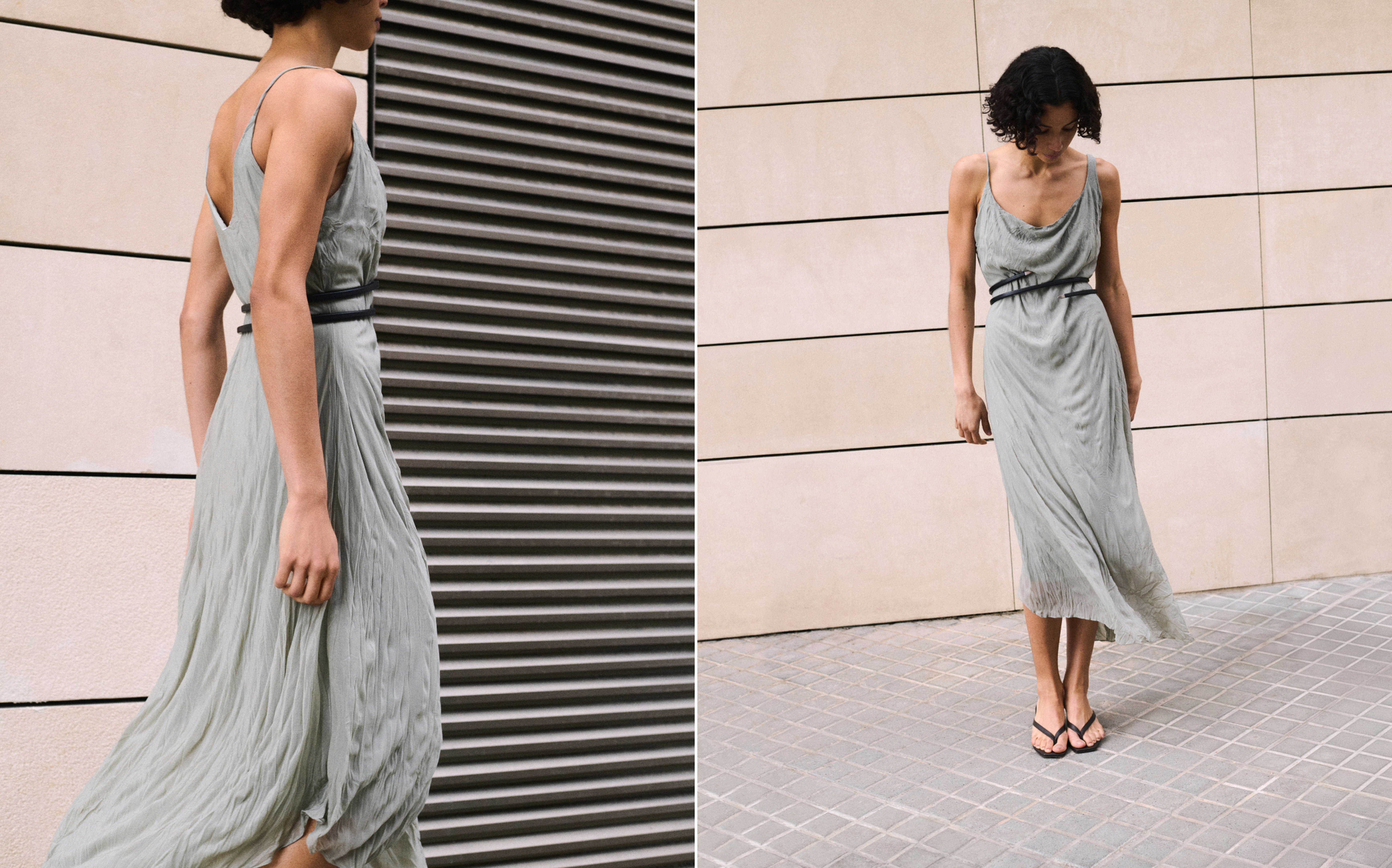 Person in a flowing gray dress with black straps and flip-flops poses against an urban backdrop with tiled and striped walls.