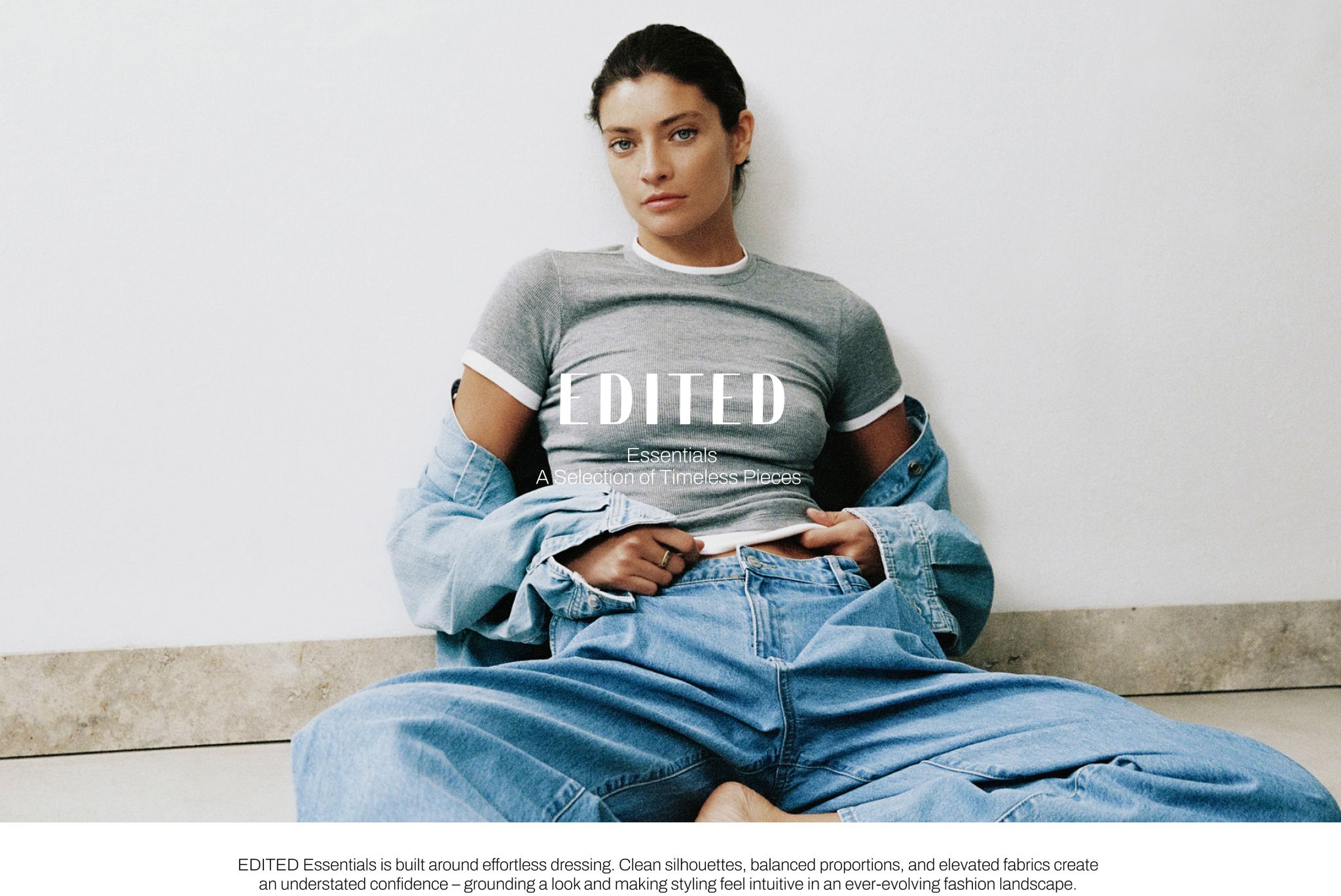 Woman in casual outfit with white shirt and grey top, denim jacket draped, sitting against a wall on a marble floor. Text overlaid at center.