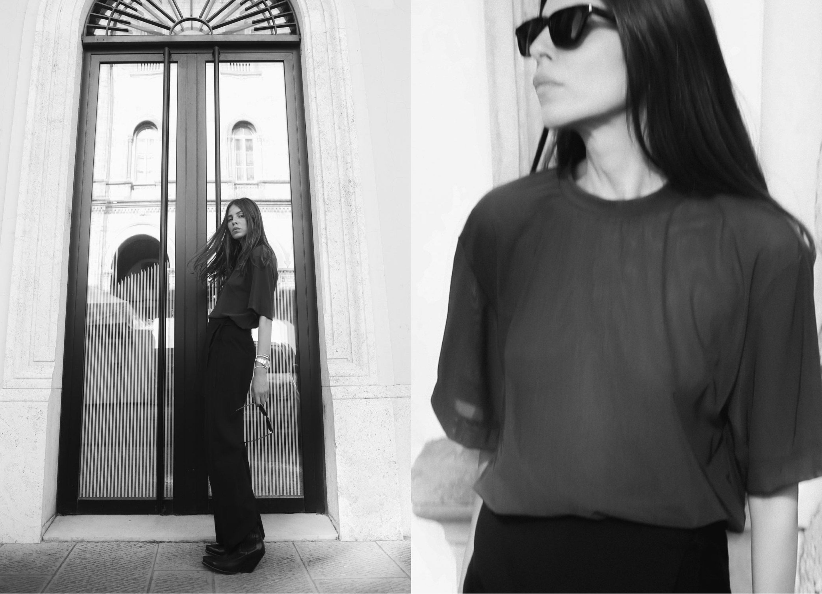 Black and white image of a woman in a dark outfit and sunglasses, standing by a tall glass door.