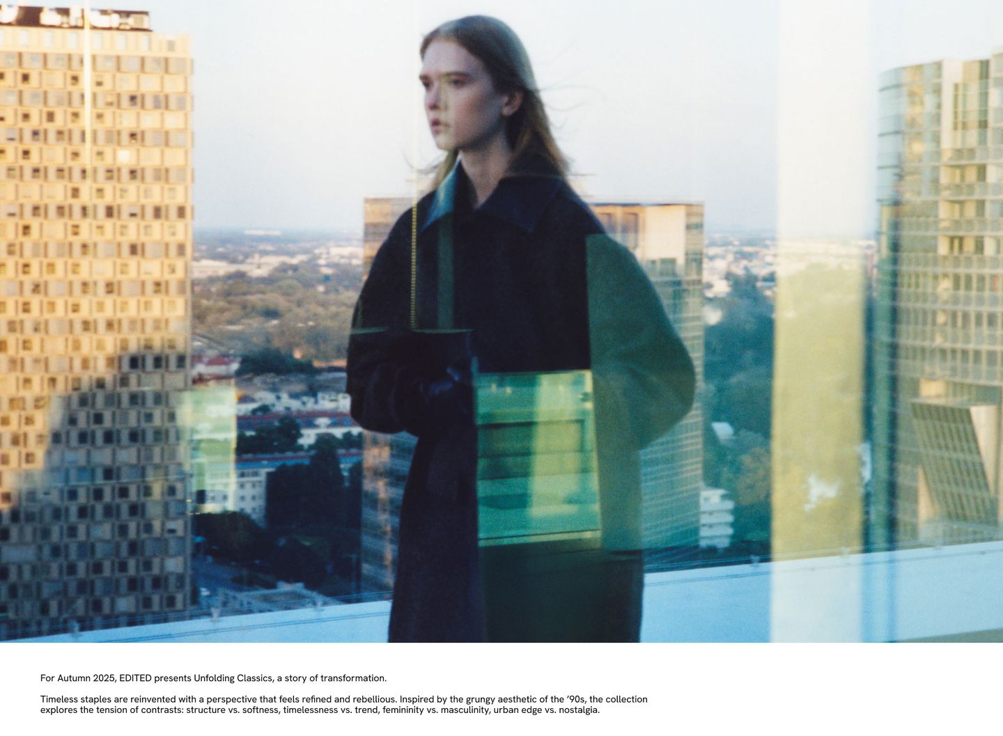 A woman in a dark coat stands on a rooftop, overlooking a cityscape with modern buildings. The image has a reflective, blurred effect.