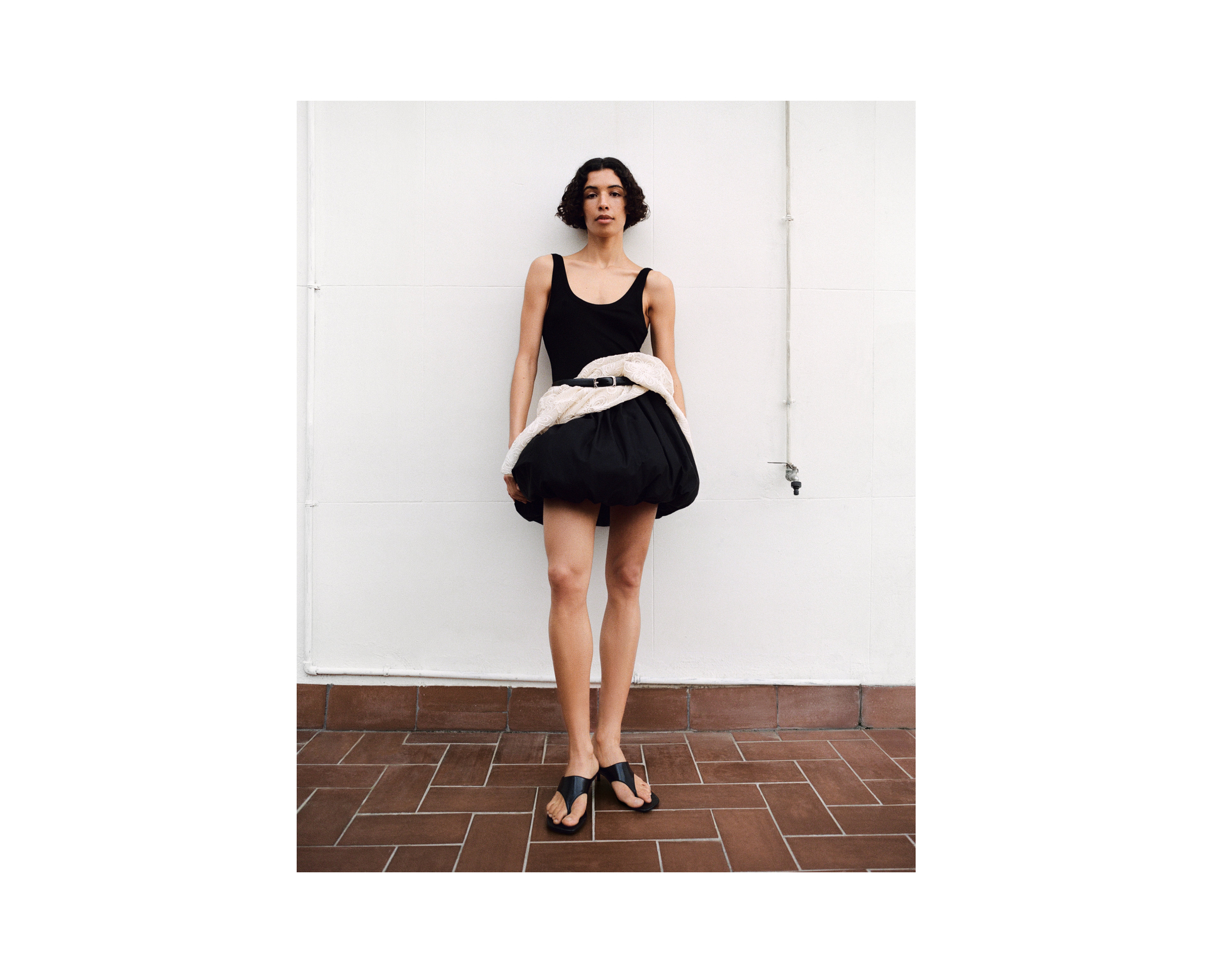 Person in a black dress with a unique white and black skirt, standing on a tiled floor against a plain white wall.