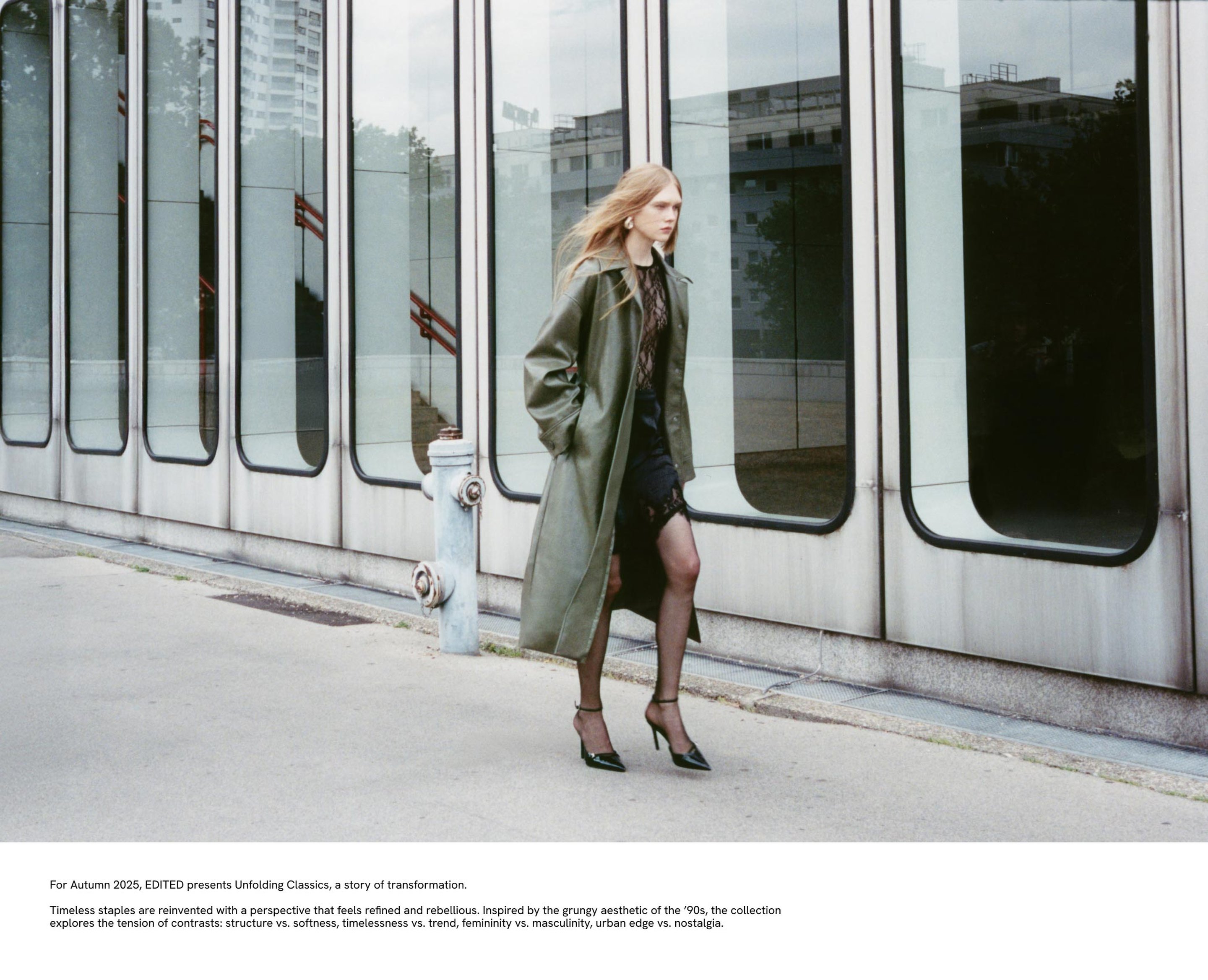 Person in a long green coat and heels walks past modern glass building. Text at bottom describes a fashion collection theme.