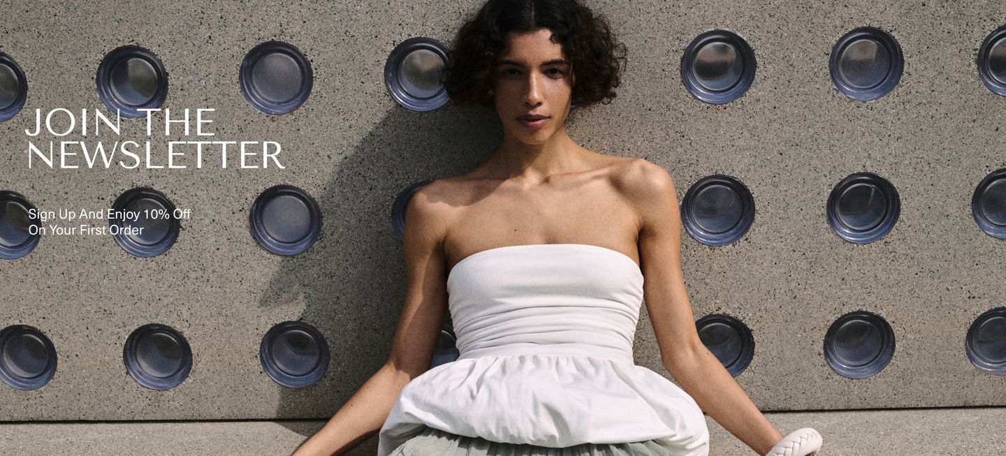 Woman in a white strapless dress sits against a textured wall with circular patterns, promoting newsletter signup for 10% off first order.