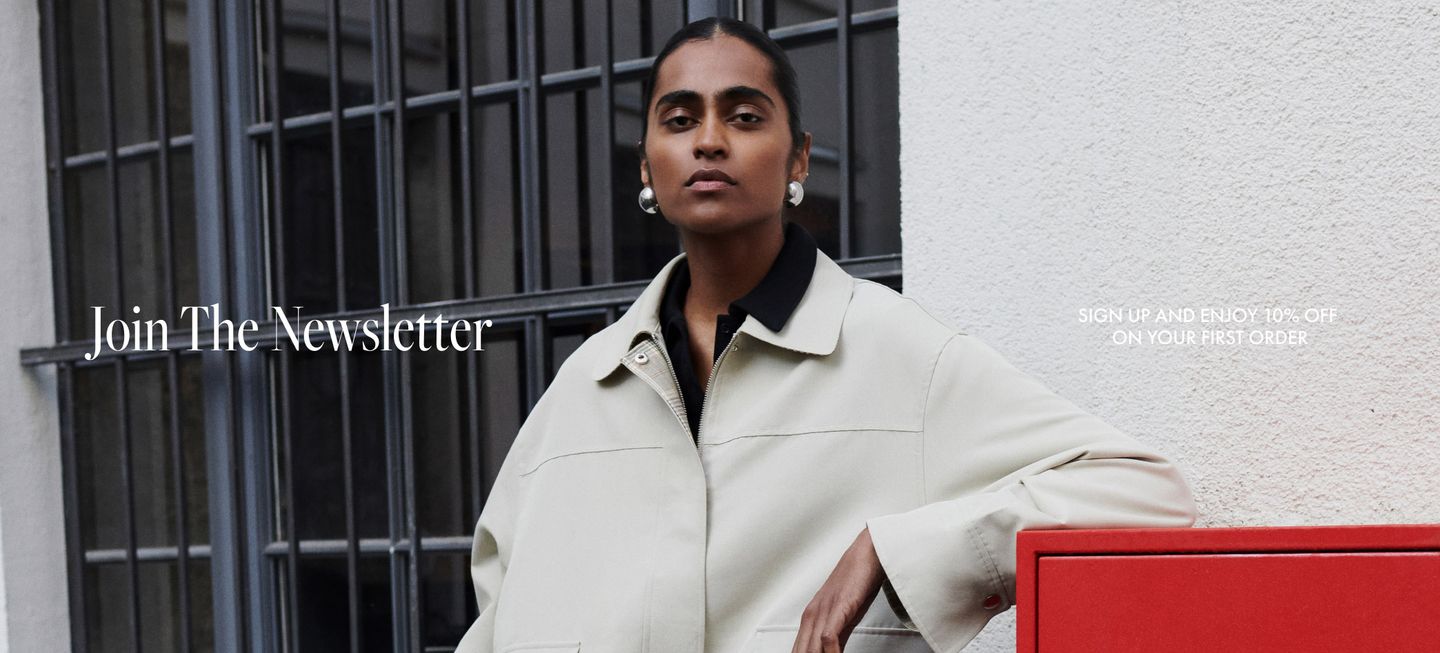 Person in a light coat stands confidently by a red postbox in front of a building. Text reads: "Join The Newsletter."