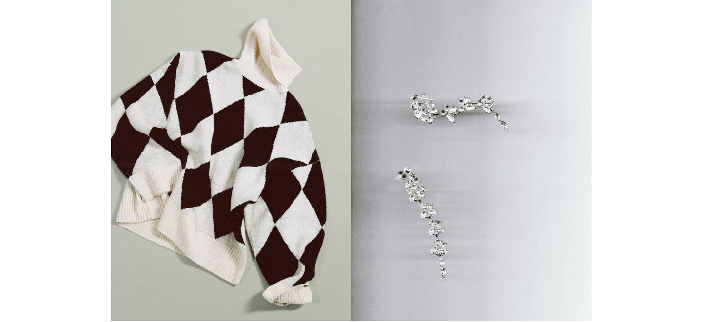 Flatlay of a cream-and-black argyle turtleneck sweater beside two silver crystal floral hairpins on split pale green and gray background.