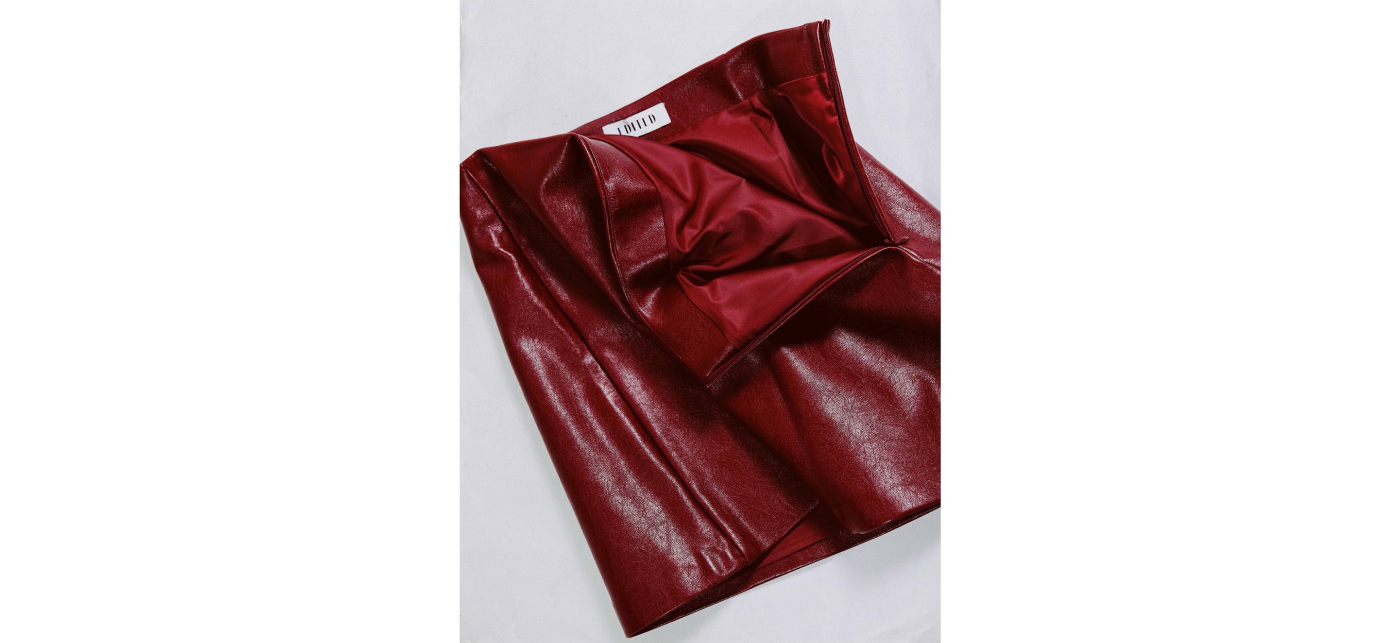 Folded shiny burgundy leather skirt with satin-like red lining and side zipper laid flat on white background.