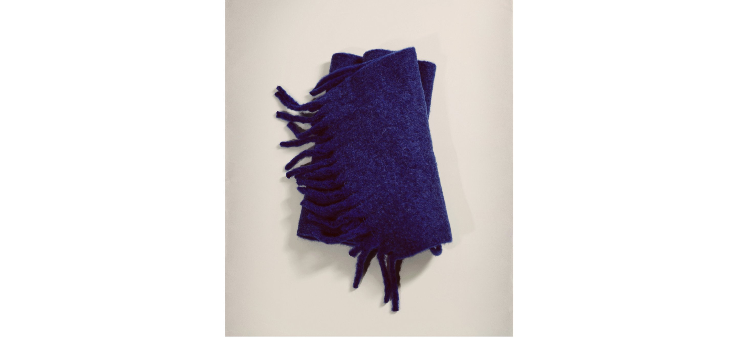 A folded blue scarf with fringed edges on a light background.