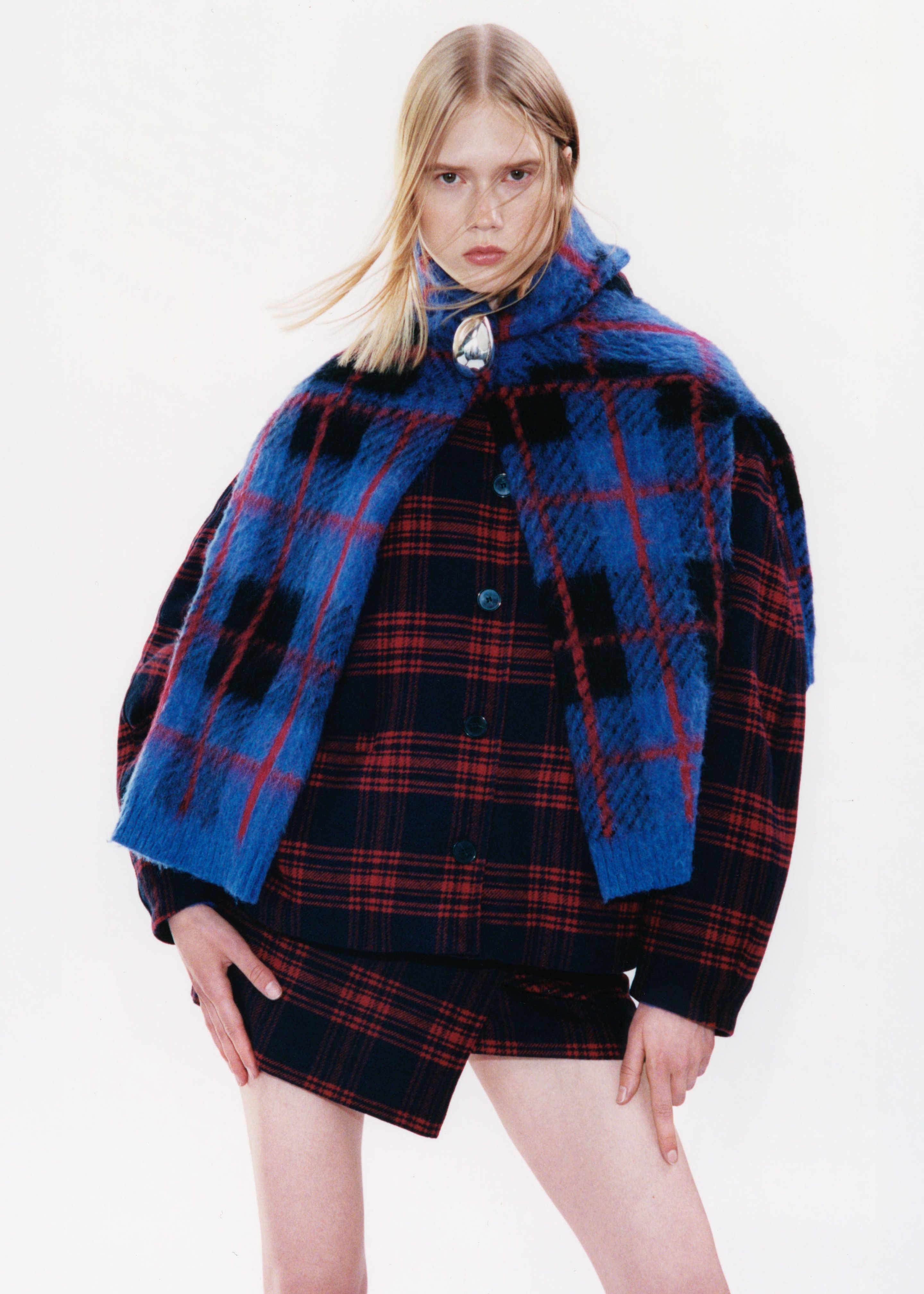 Person wearing a blue and red plaid outfit with a matching scarf, standing with hands on hips against a plain background.