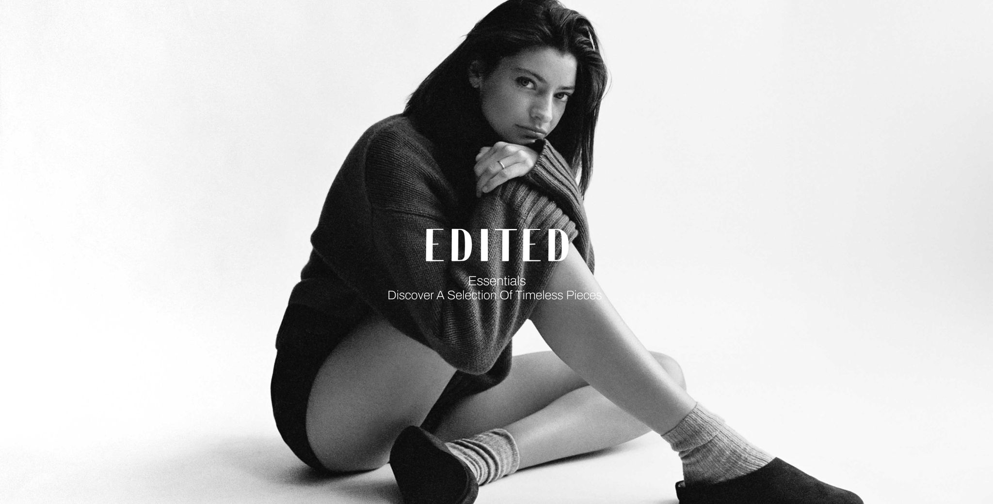 Black and white image of a woman sitting on the floor in a cozy sweater, socks, and shoes, gazing thoughtfully at the camera. Text overlays are present.