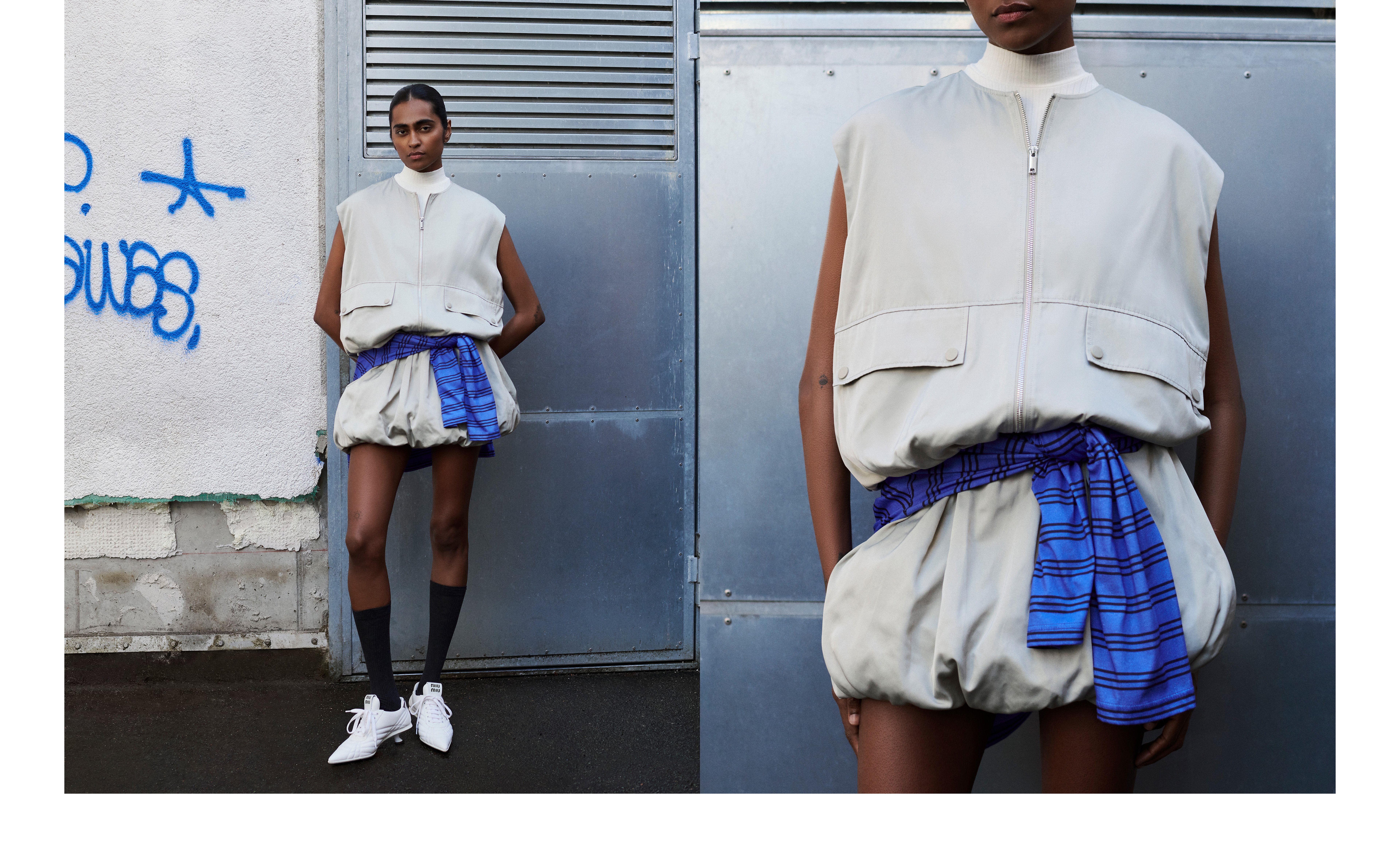 Person in a beige sleeveless top and shorts, with a plaid blue shirt around the waist, stands near a wall with graffiti and metal shutters.