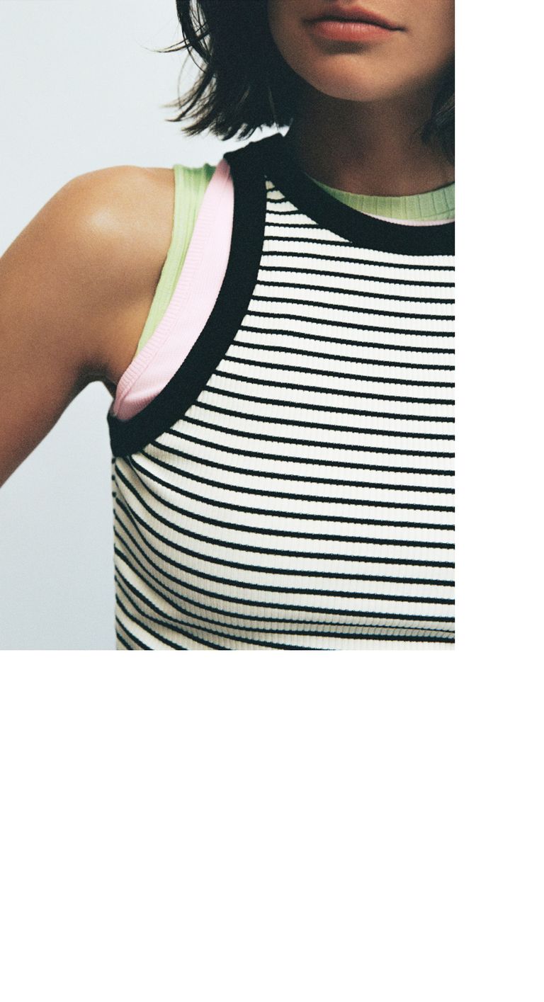 A woman in a striped sleeveless top with green and pink layers, short hair visible, against a neutral background.