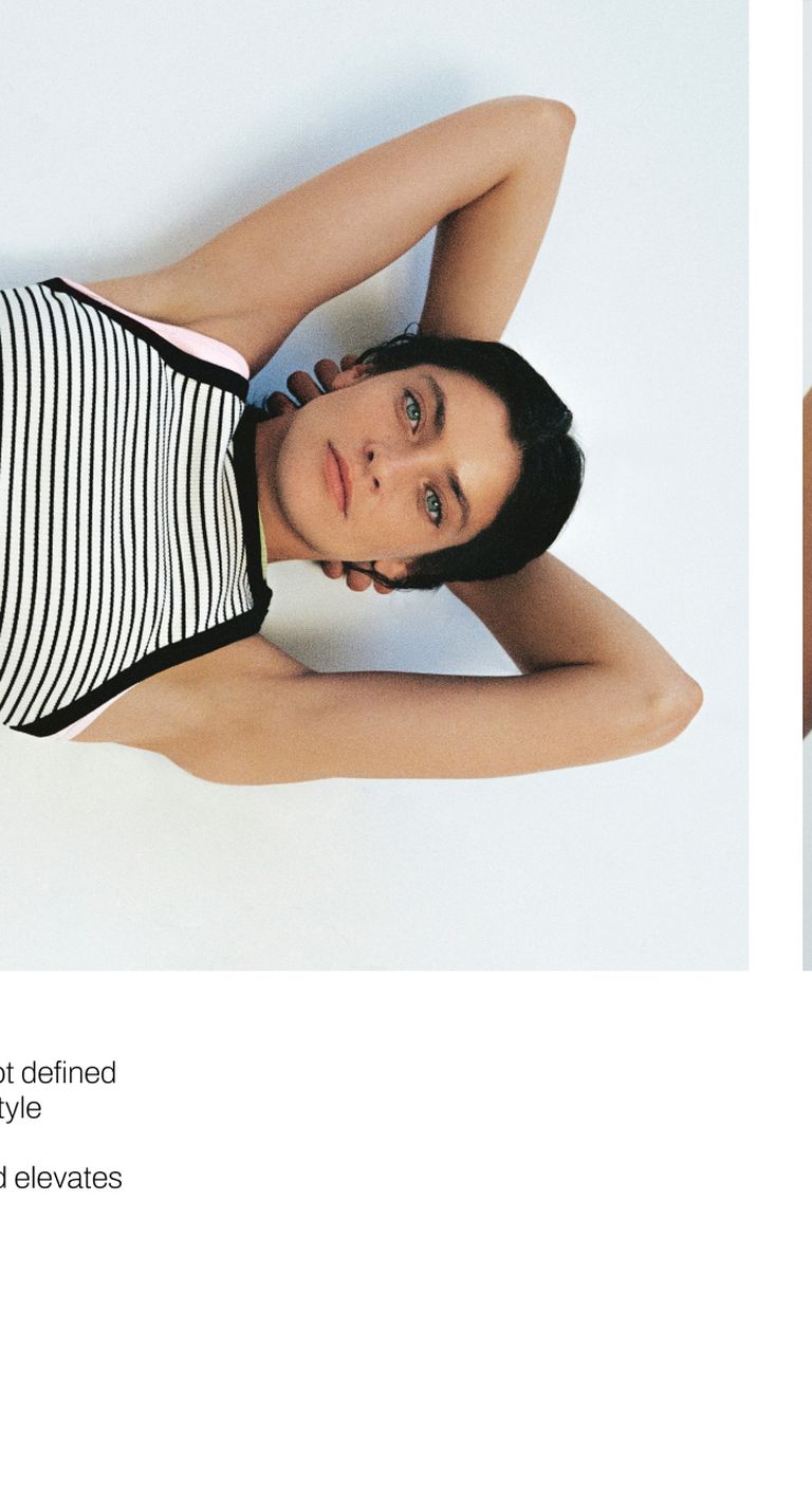Person with dark hair and striped top lies on a white surface, arms resting behind their head, gazing upward.