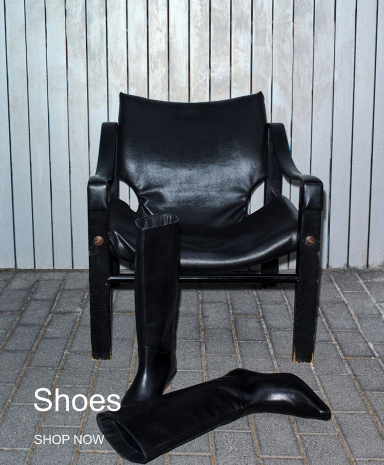 Black leather chair with tall black boots placed in front, against a wooden plank wall. Text reads: "Shoes, Shop Now."