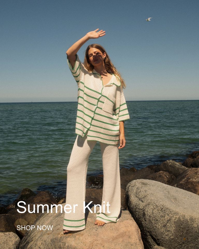 Woman in a white and green striped knit outfit stands on rocks near the ocean, shielding her eyes from the sun. Text reads "Summer Knit, Shop Now."
