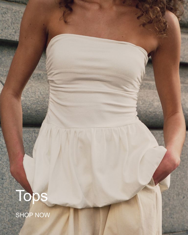 A person in a strapless white peplum top stands with hands in pockets. Text on the image reads "Tops" and "Shop Now."