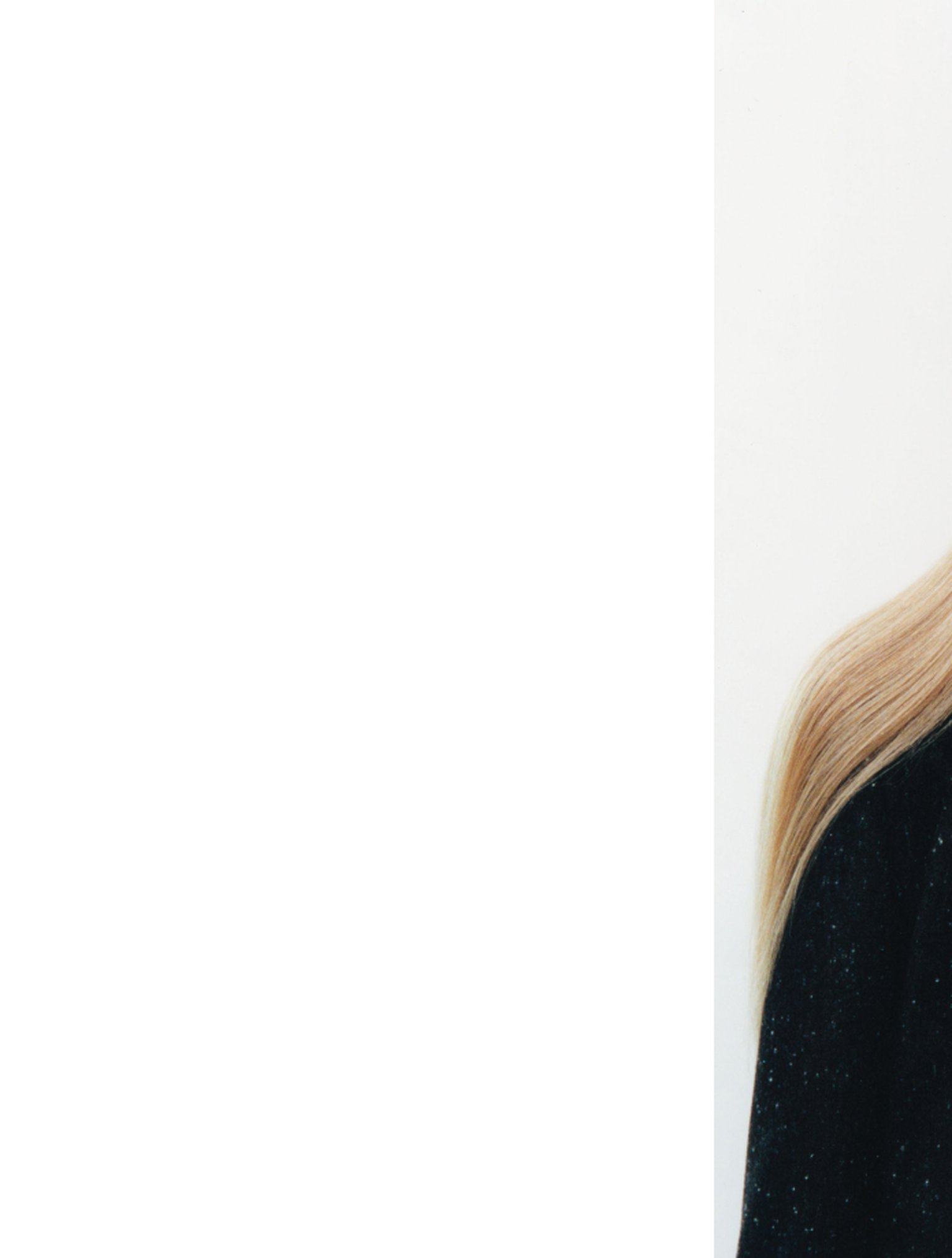 Close-up of a person with long, straight blonde hair wearing a black speckled sweater against a plain white background.