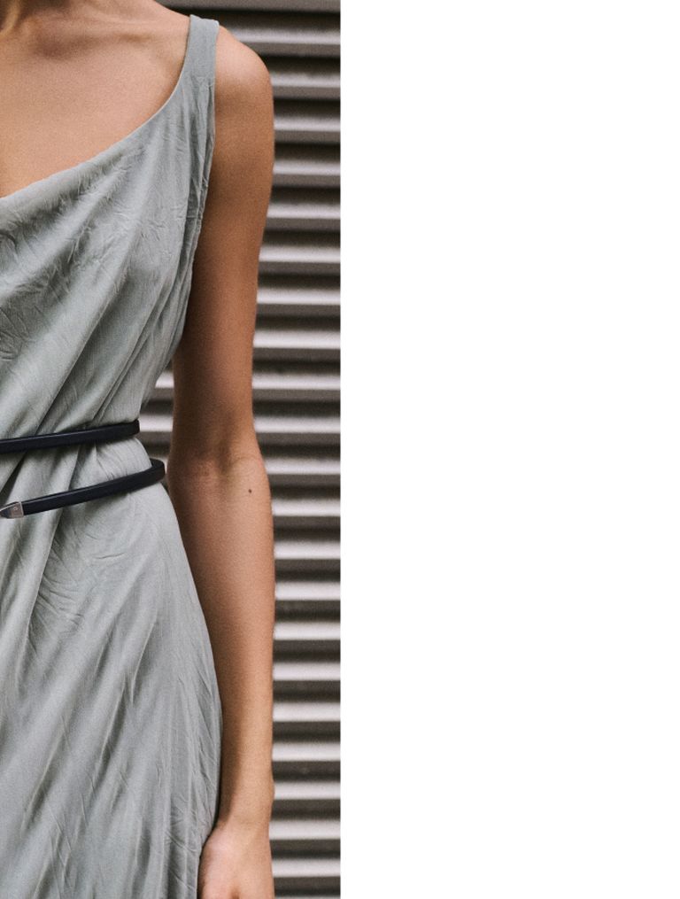 Person in a light gray sleeveless dress with a slim black belt, standing against a metal shutter background.
