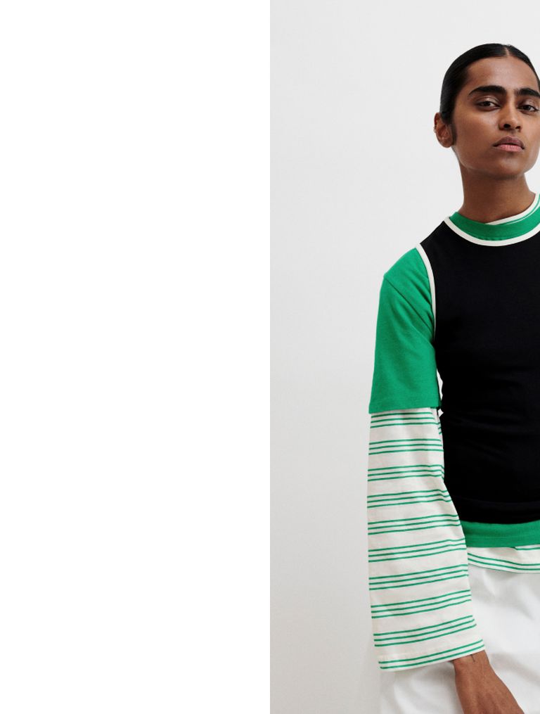 Person in a layered outfit with black, green, and striped sleeves, standing against a plain background.