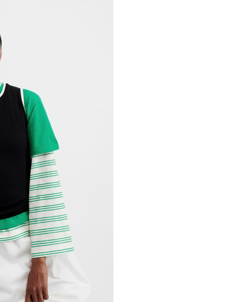 Person wearing a layered outfit with a green shirt, black top, and striped sleeves, against a white background.
