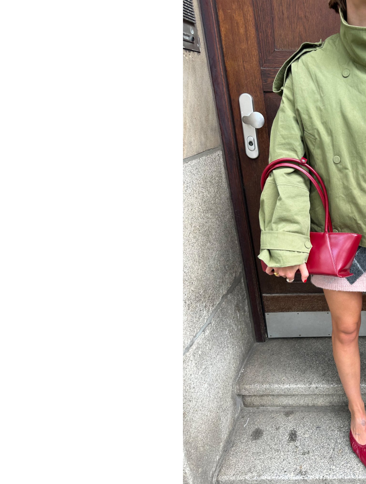 Person in oversized green jacket holds a small red handbag, standing on stone steps by a wooden door.
