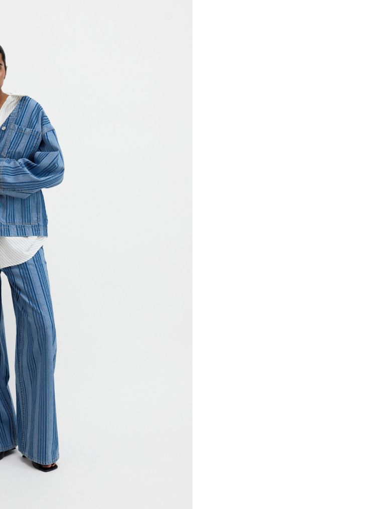 Person wearing a blue denim jacket and pants, with a white shirt underneath, standing against a plain white background.