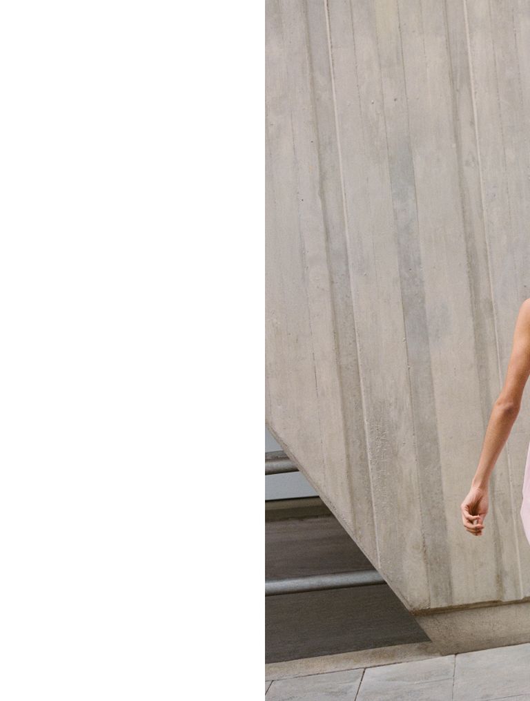 A person in a white shirt and tie stands next to a slanted concrete wall outdoors. Only the right arm is visible.