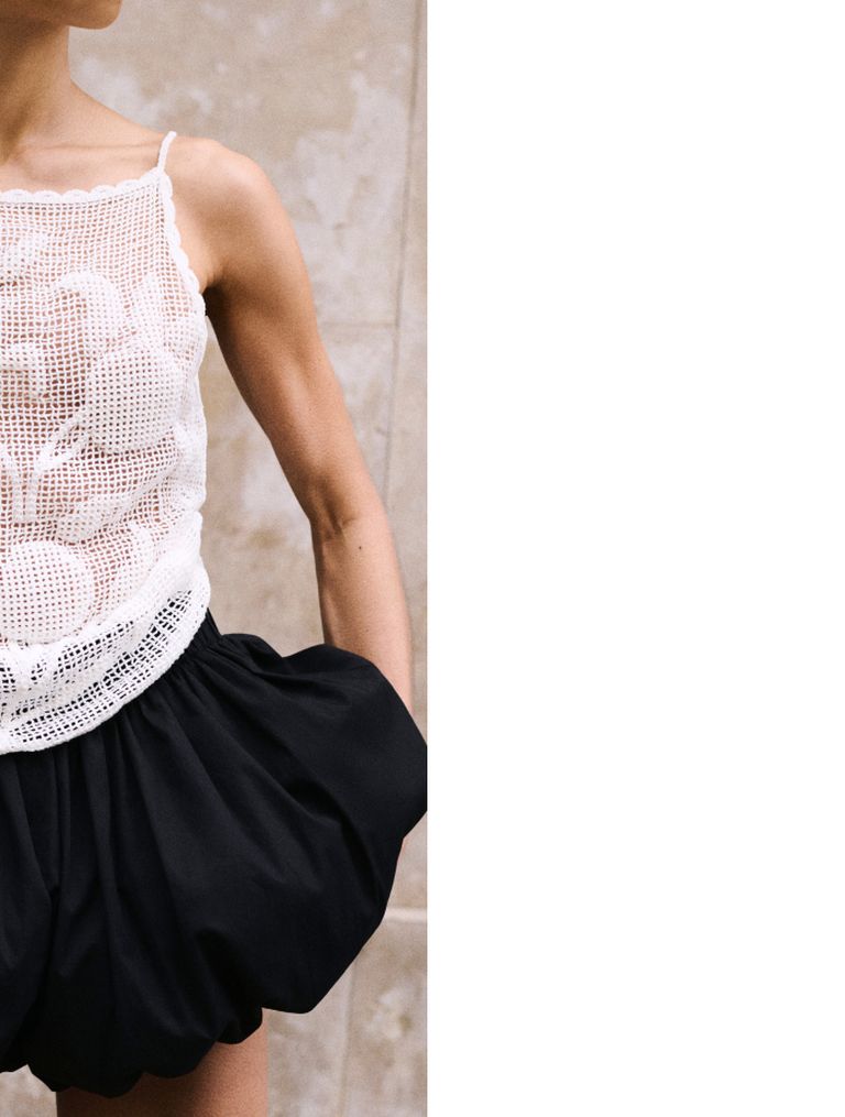 Person wearing a white crochet tank top and black skirt with bubble silhouette, standing against a neutral background.