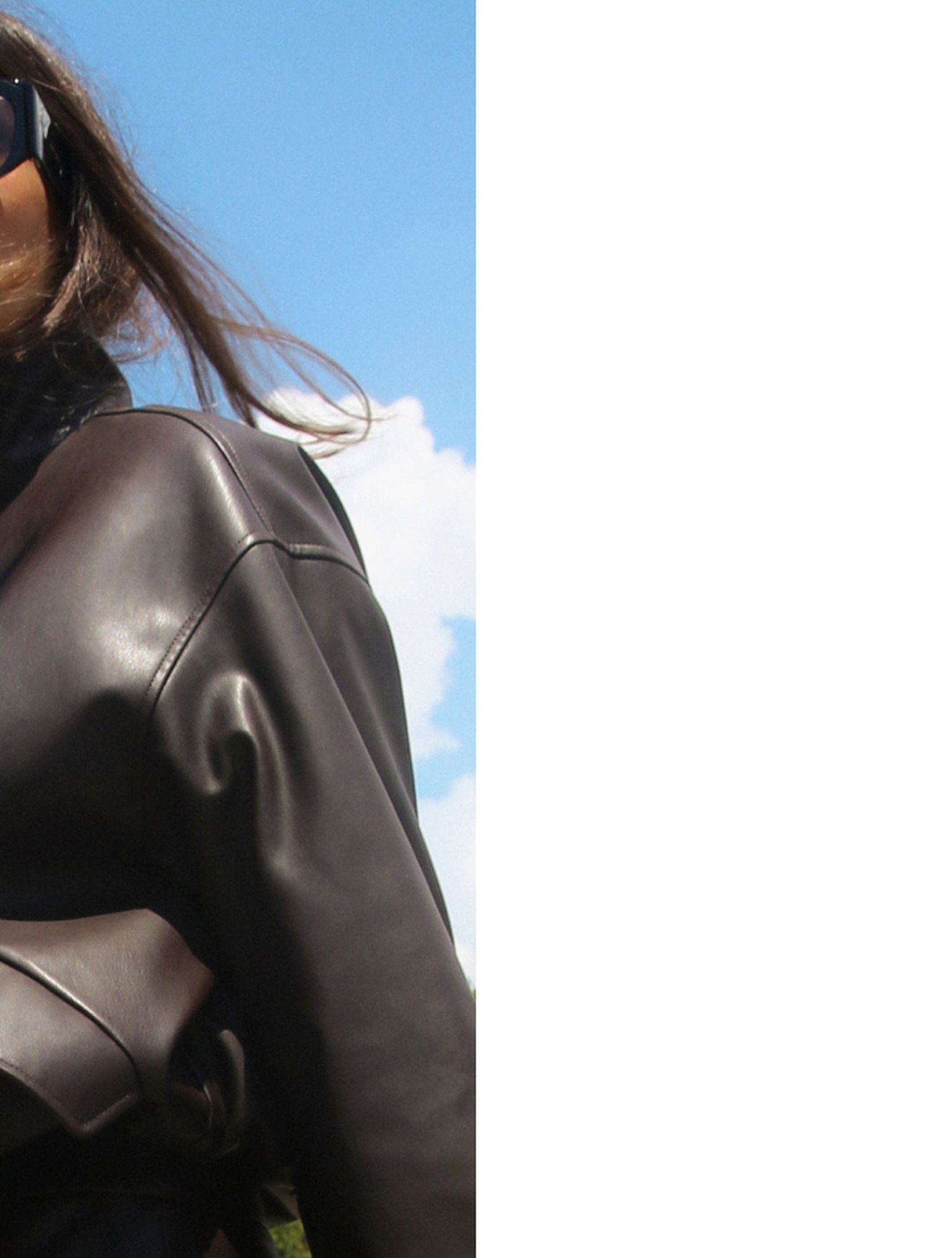 Person wearing a black leather jacket and sunglasses against a blue sky background.