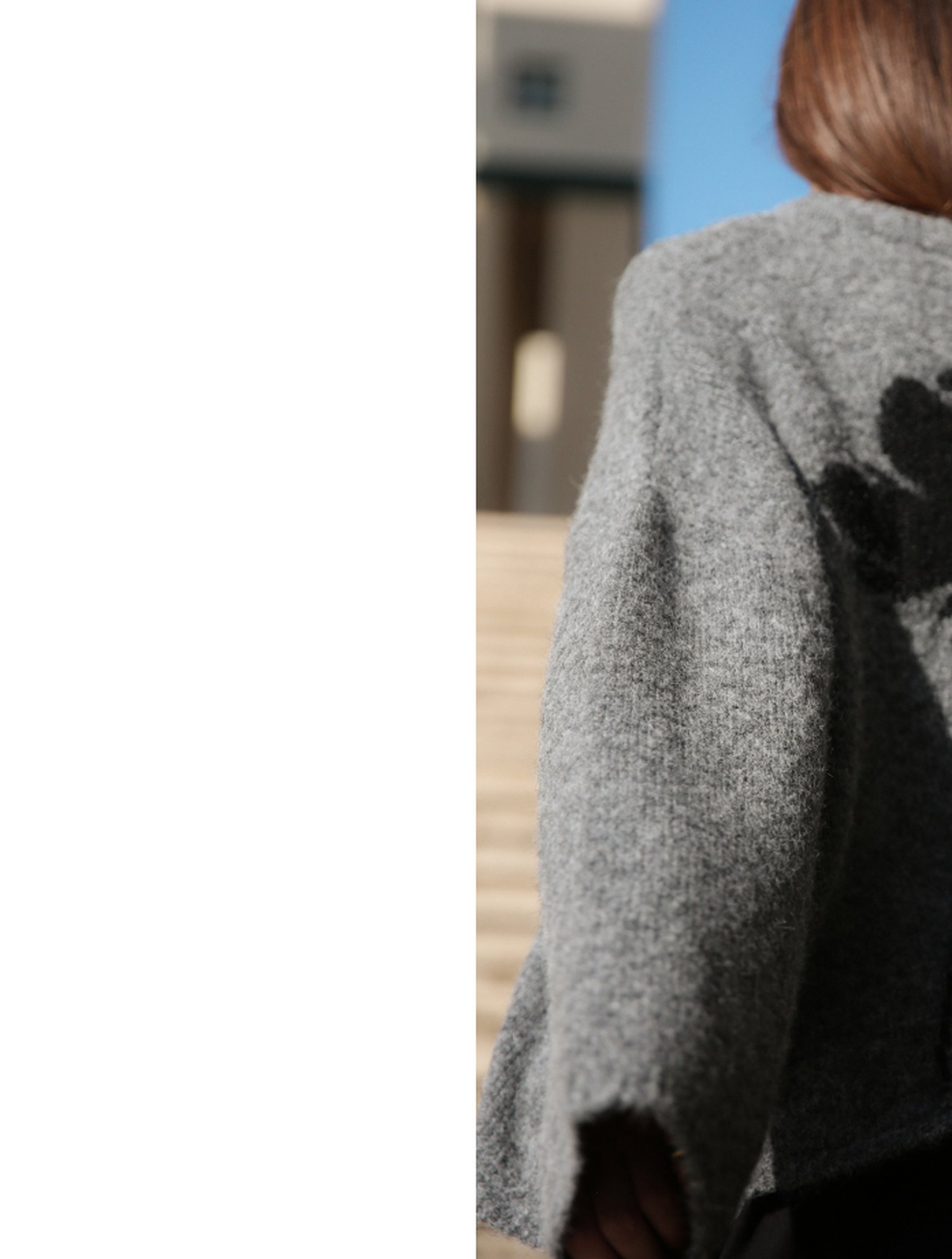 Person in a gray sweater standing outside, with a shadow of a hand on their back. Background includes steps and a building.