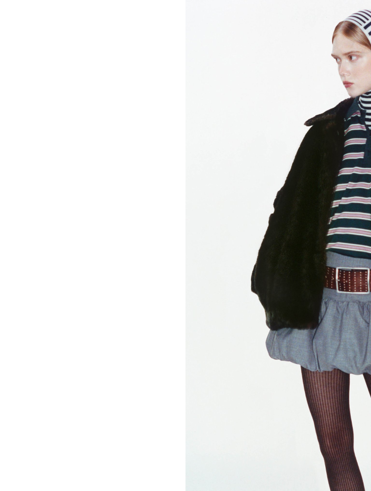 Person wearing a striped shirt, black jacket, and skirt with tights, partially visible against a white background.