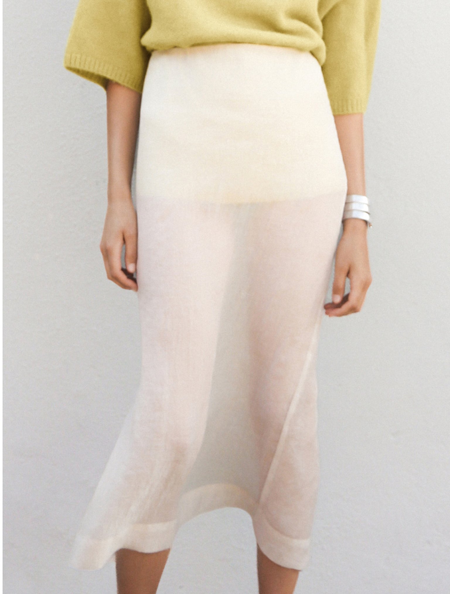 Person wearing a light yellow top and a sheer white skirt, standing against a plain white background.