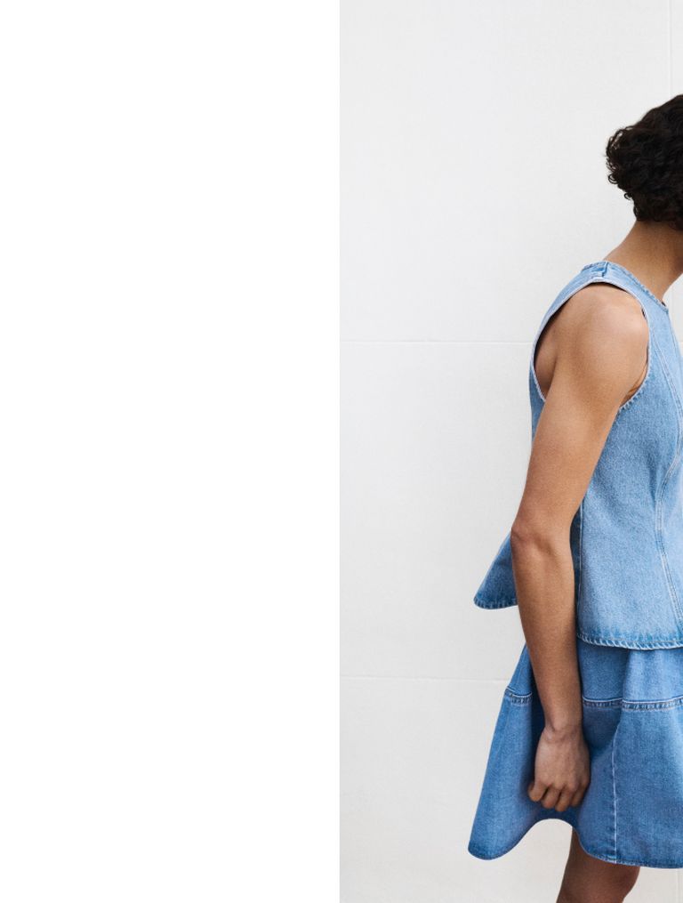 Person in a sleeveless denim dress stands against a plain white background, with visible shoulders and back.