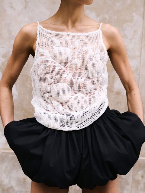 Person wearing a white crochet top and black bubble skirt, standing against a neutral background.