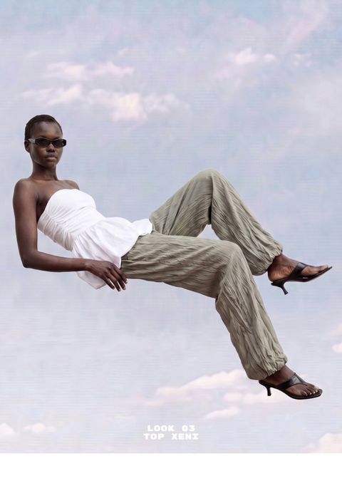 Model in a white strapless top and green pants, wearing sunglasses and heels, appears to float against a cloudy sky backdrop.