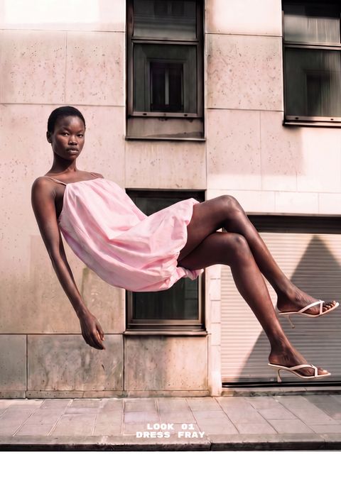 Model in a pink dress levitates against a city building backdrop, wearing white heels. Text: "LOOK 01 DRESS FRAY".