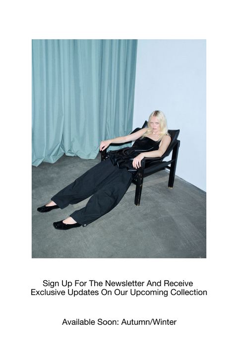 A person in black clothing relaxes on a chair in a minimalist room with teal curtains. Text promotes a newsletter for an upcoming collection.