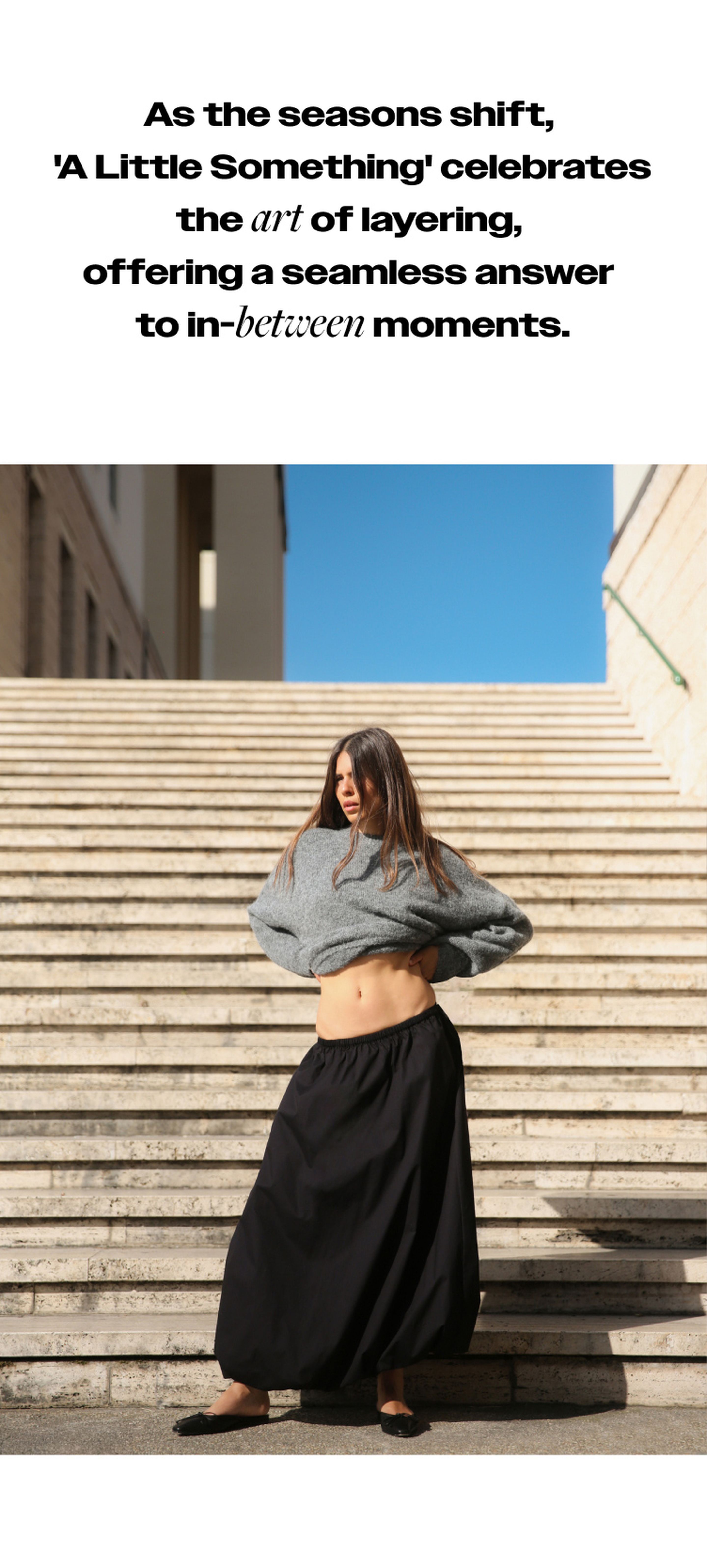 Woman in a gray sweater and black skirt adjusts her outfit on outdoor steps. Text above discusses layering for transitional seasons.
