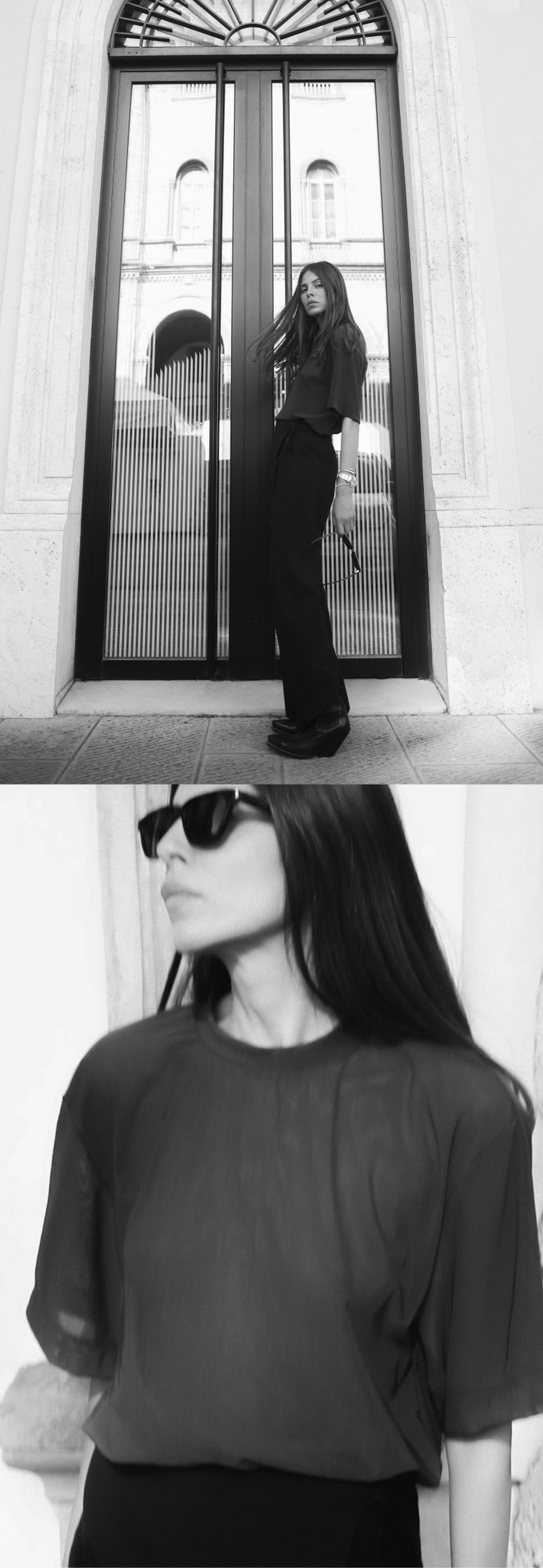 A woman in a sheer top and wide-leg pants poses confidently by a tall glass door, wearing sunglasses and looking away. Black and white image.