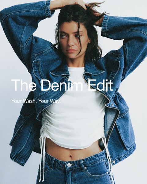 Woman in a denim jacket and jeans poses with arms raised, wearing a white top. Text reads “The Denim Edit. Your Wash, Your Way.”