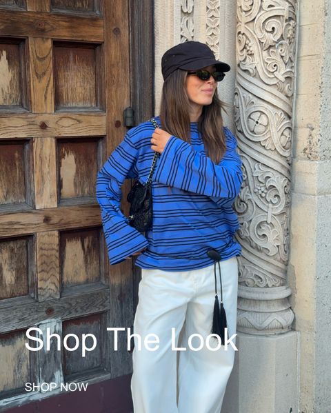 Woman in blue striped top, white pants, black cap and sunglasses leans against ornate wall. Text reads "Shop The Look."