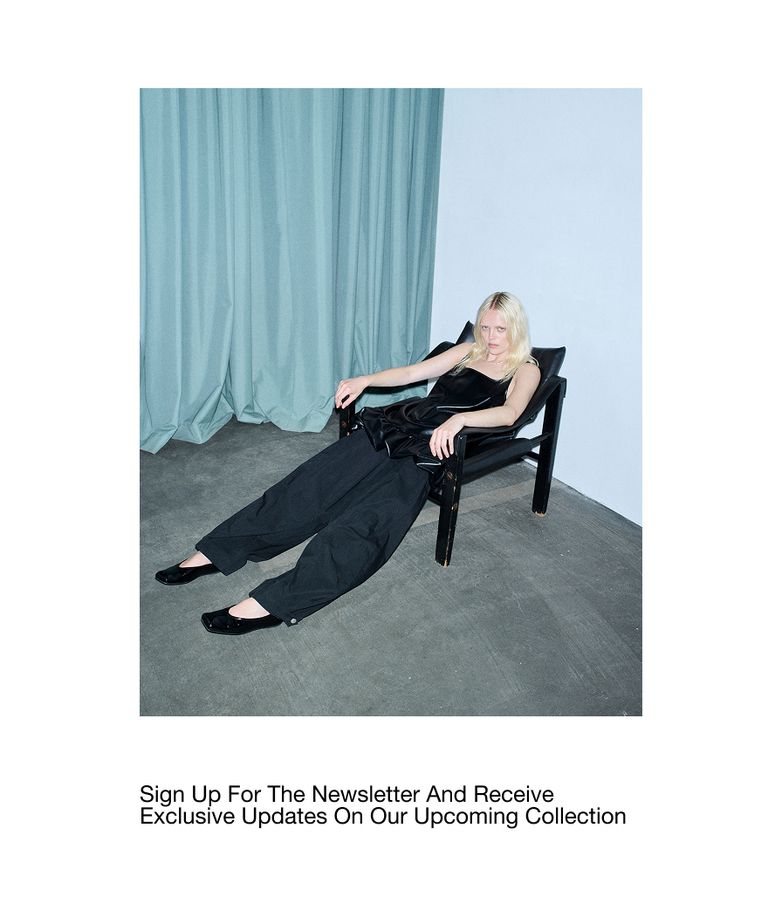 Person in black outfit reclining in a chair against a backdrop of teal curtains with text about signing up for a newsletter.