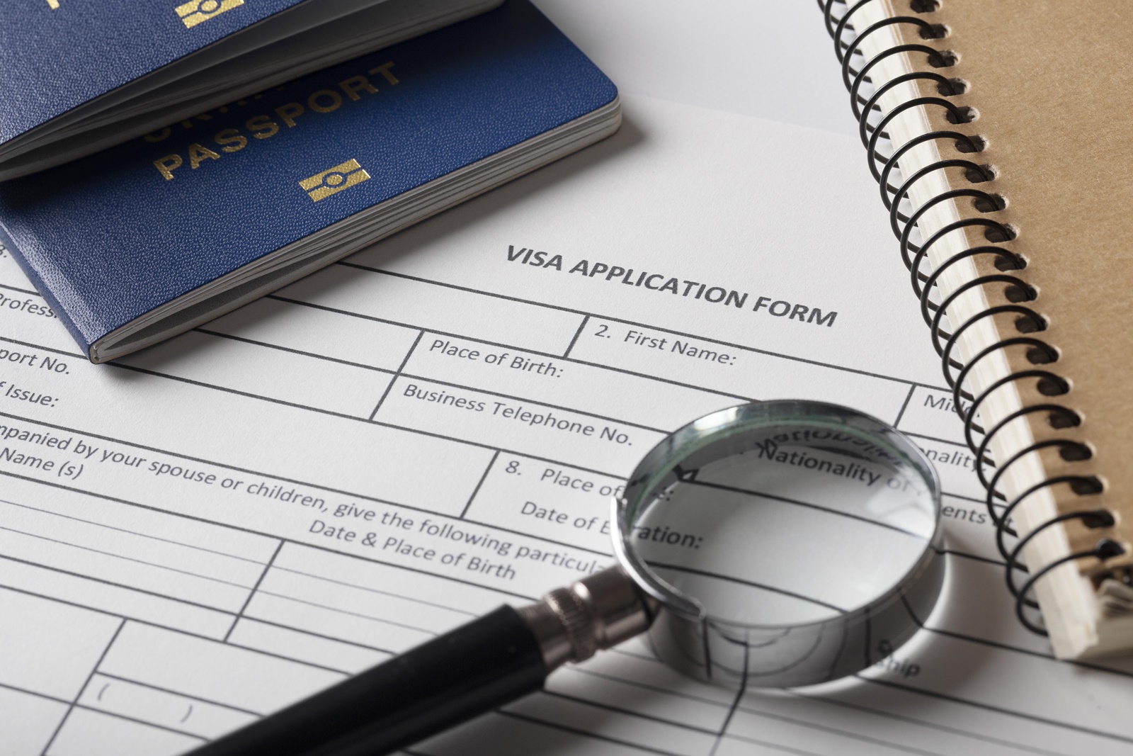 Visa Application Form Visa application form with a magnifying glass on top, next to a blue passport and a spiral notebook.