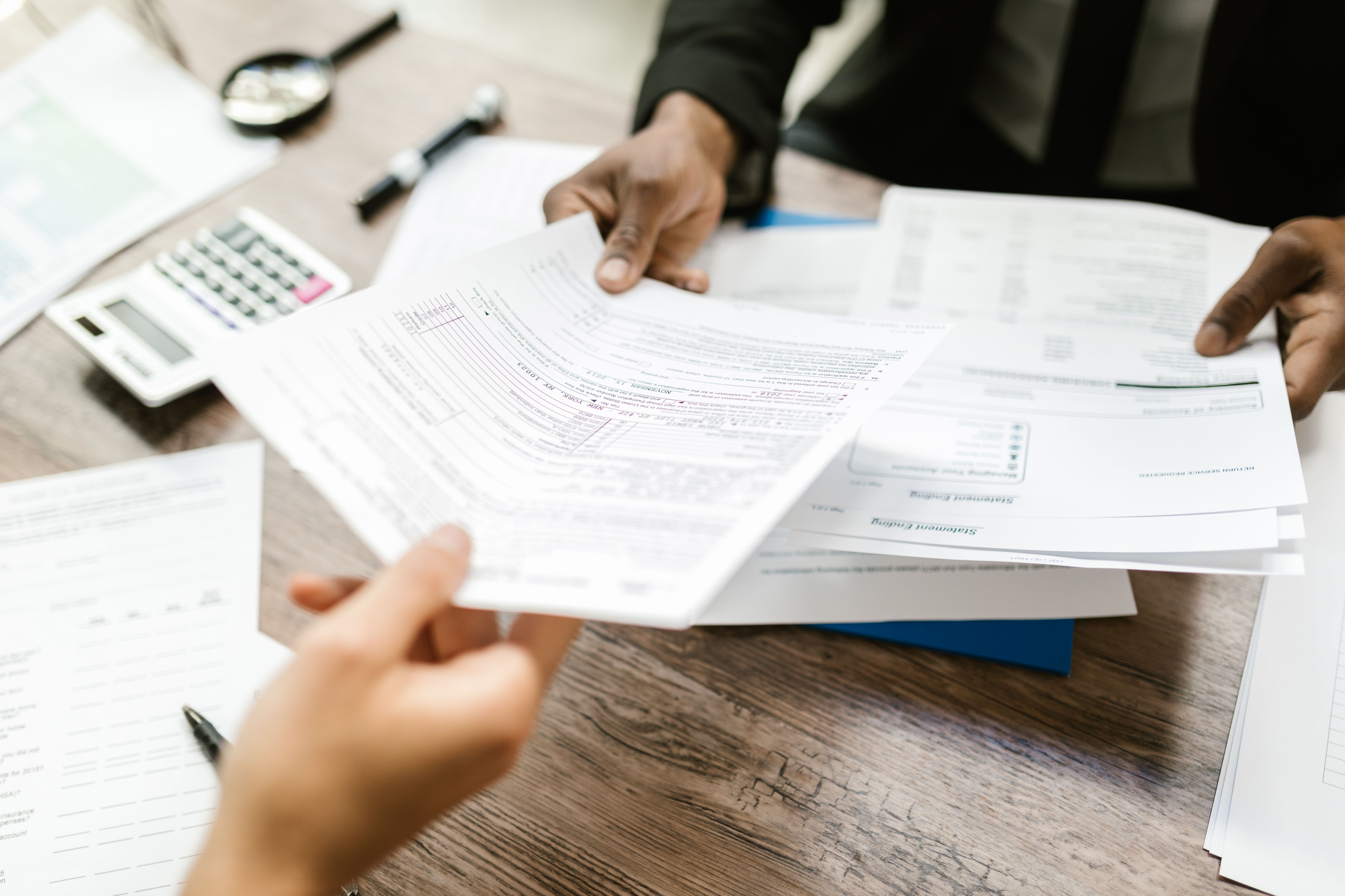Tầm quan trọng của Visa Two people exchanging documents over a table, with a calculator and other papers scattered around.