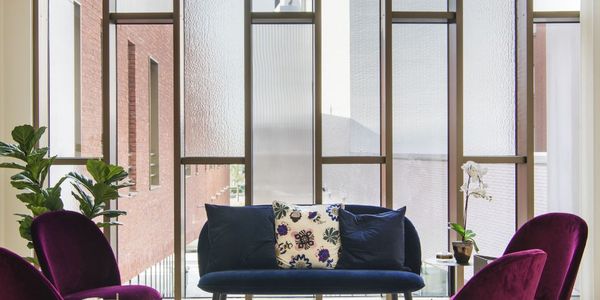 Moderne Lounge mit hohen Milchglasfenstern, violetten Stühlen, einem blauen Sofa, einem gestreiften Teppich und der ONE 60 Pendelleuchte.