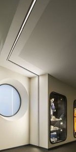 Ein modernes Interieur mit einem runden Fenster und eingelassenen Vitrinen, in denen die Exponate unter sanfter Beleuchtung präsentiert werden, sowie einer klaren, minimalistischen Deckenstruktur. Die 48-V-Schiene verläuft entlang der Wand und fügt sich nahtlos in die Decke ein.